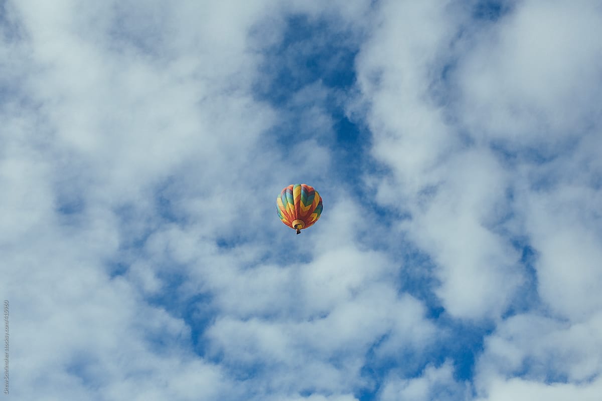 Multicolored hot air balloon in the center of a cloudy, blue sky