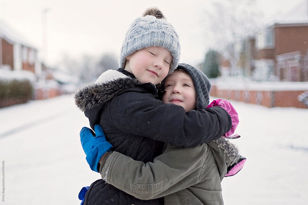 Brother and sister hug in street in snow