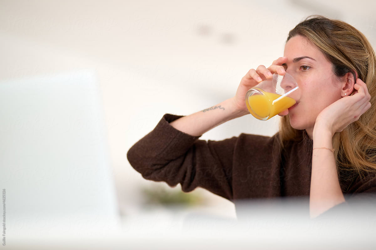 Woman drinking juice while looking at laptop.
