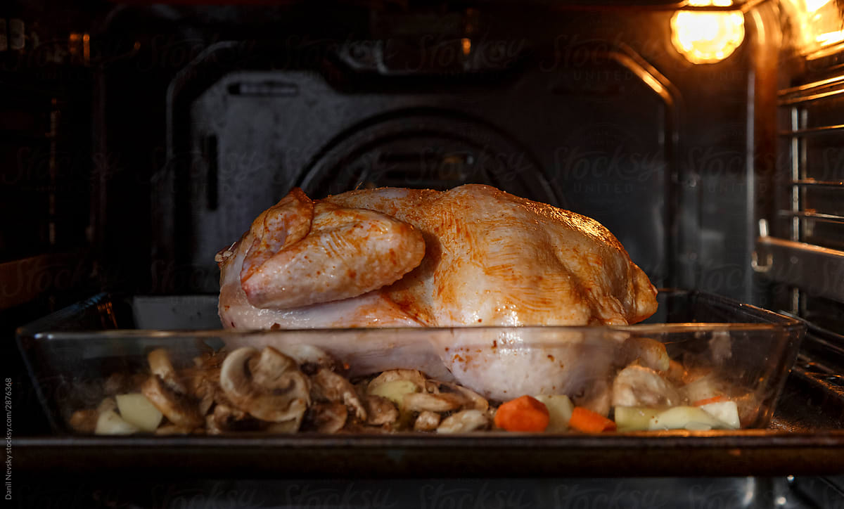 Seasoned chicken with vegetables in baking dish cooking in oven with light