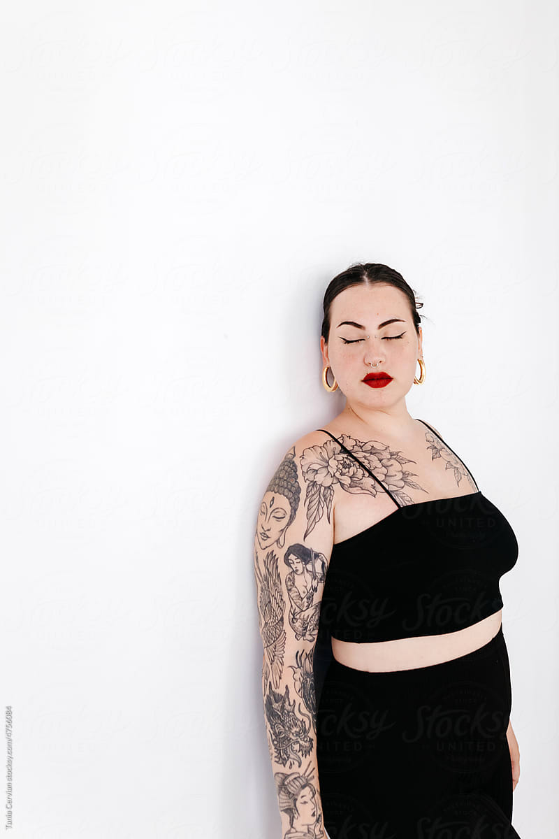 Tattooed woman standing near wall in studio