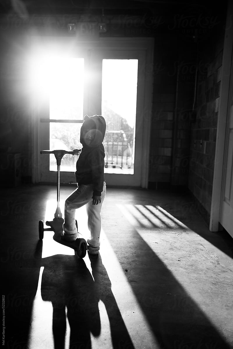 Girl on scooter in dramatic shadow light in front of glass door
