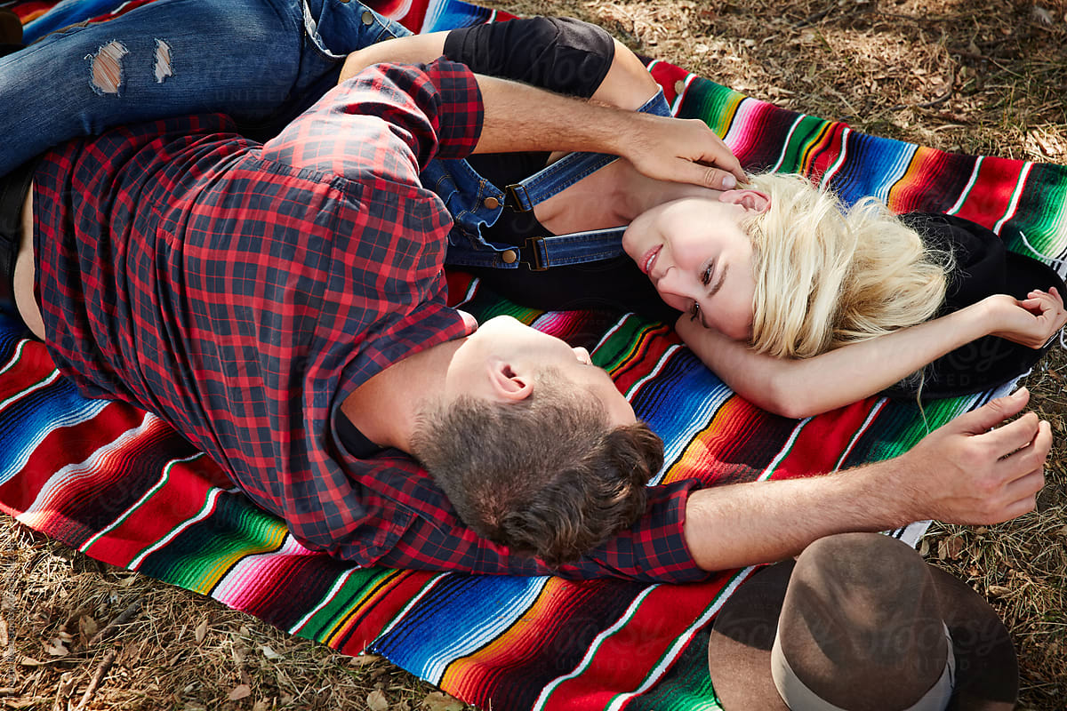 Millennial couple having a romantic moment lying on blanket in park