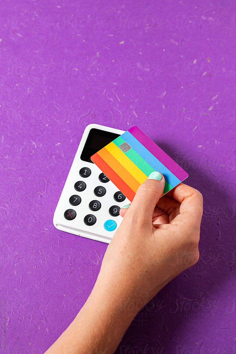 A hand paying with a credit card on the colors of the LGBTQ flag