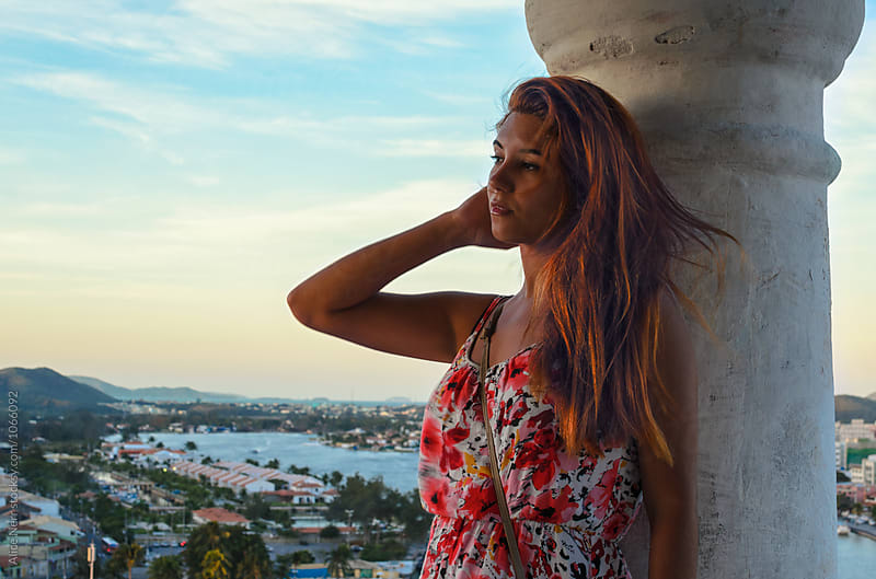 Redhead woman nest to a column with aerial view to a coastal city