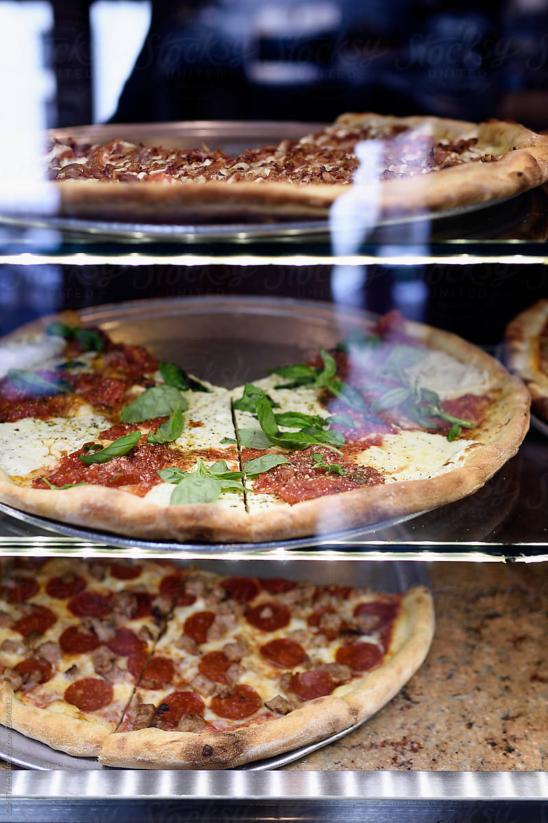 New York deli pizzas through a glass display case