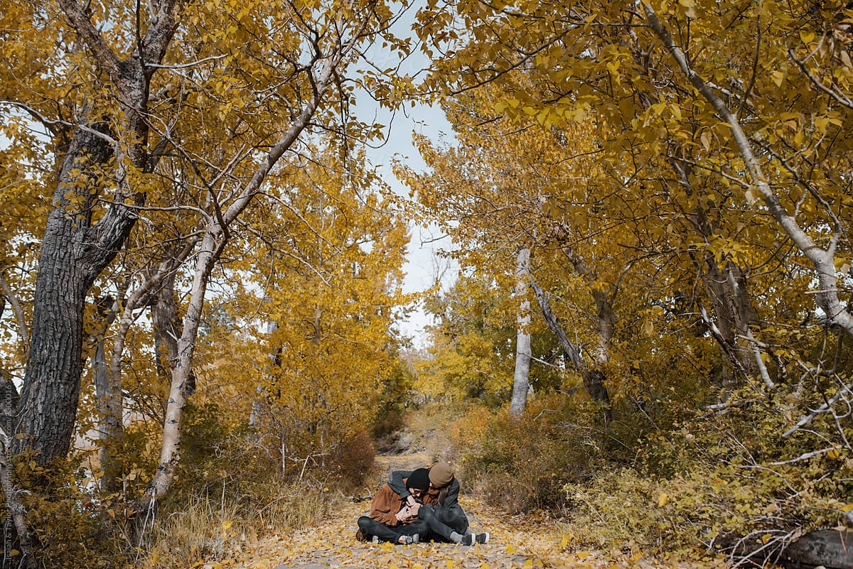 Two girls hugging and cuddling close together on the floor outdoors in nature under yellow trees