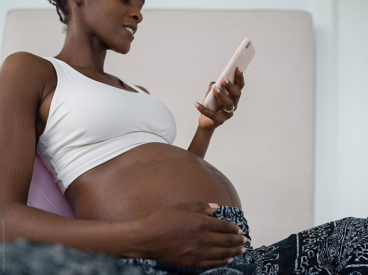 Smiling pregnant woman caressing belly and using mobile
