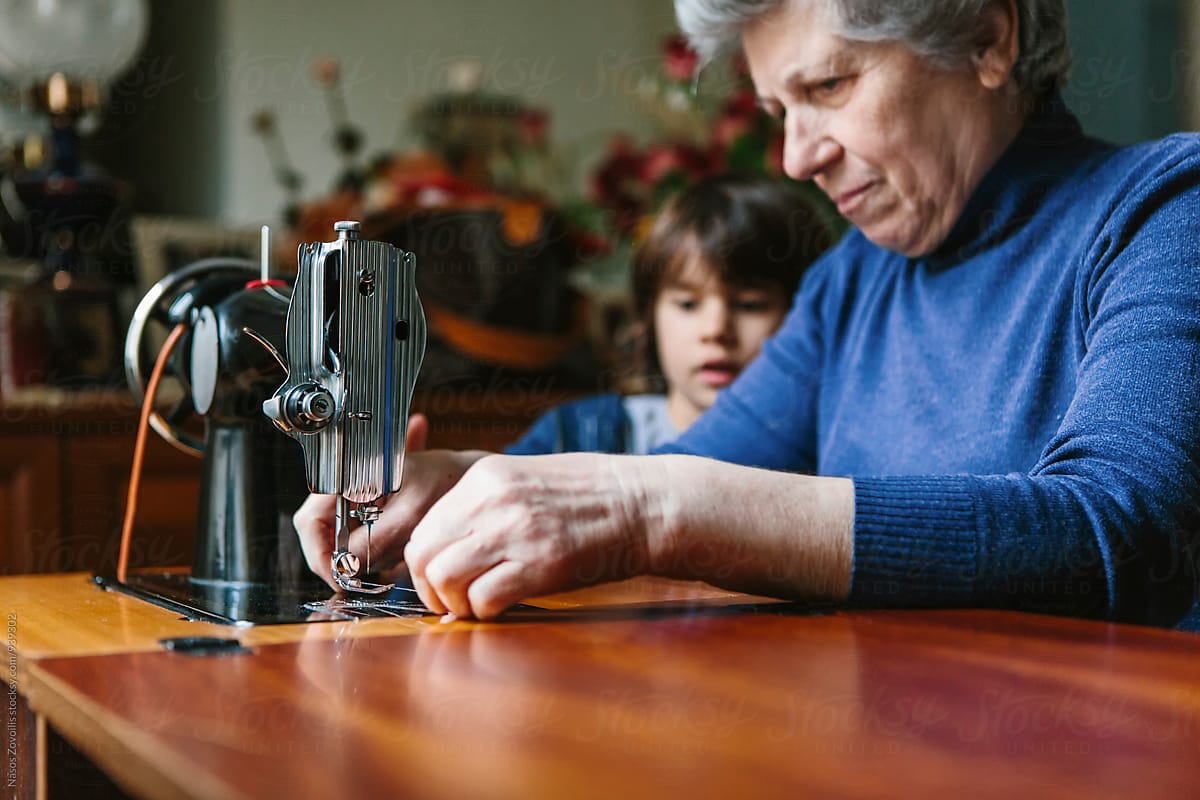 5 years old boy looking his grandmother working on a sewing machine