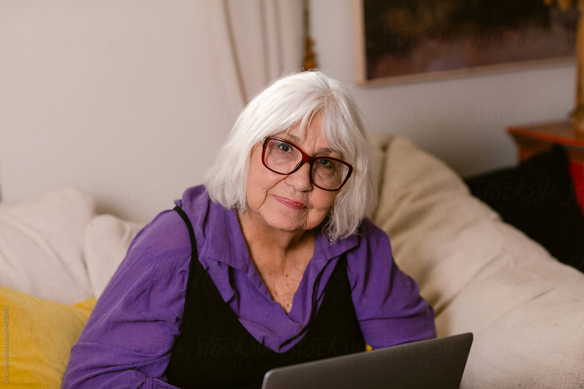 Modern elderly woman with laptop sitting at home
