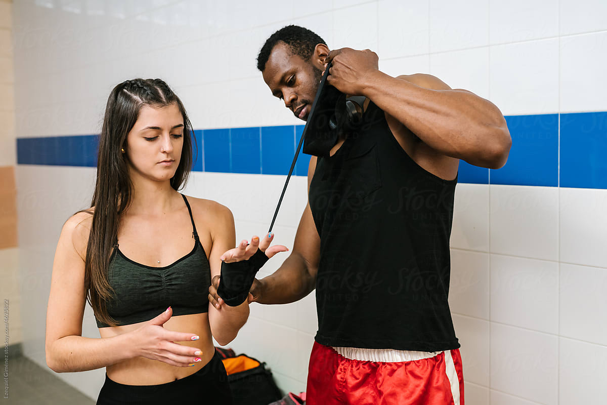 Black trainer helping female boxer to bandage hand