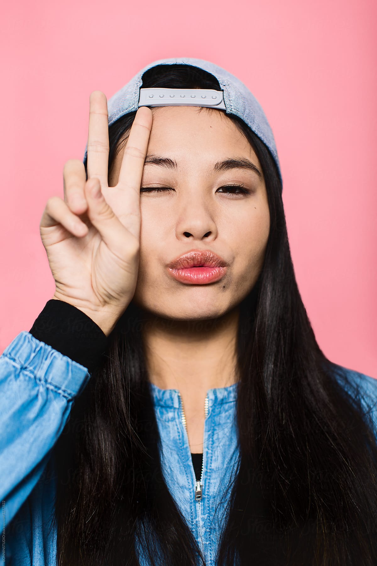 Teen asian girl giving hand sign over pink portrait.