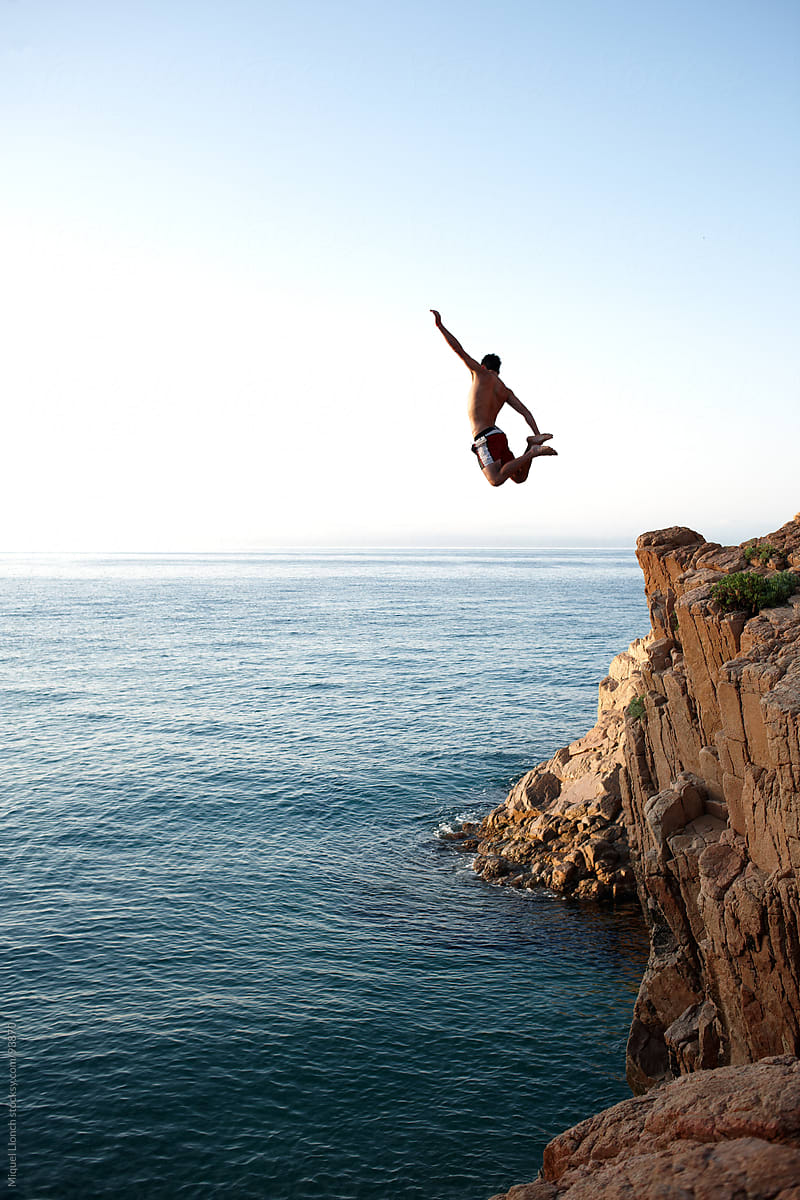 Young man jumping a cliff in a blue sea and sky