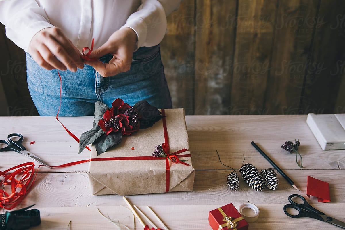 Woman decorating Christmas present with red ribbon