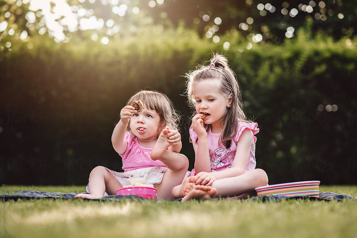 Two Cute Girls Outdoors Sitting On The Grass Having A Snack By Lea Csontos