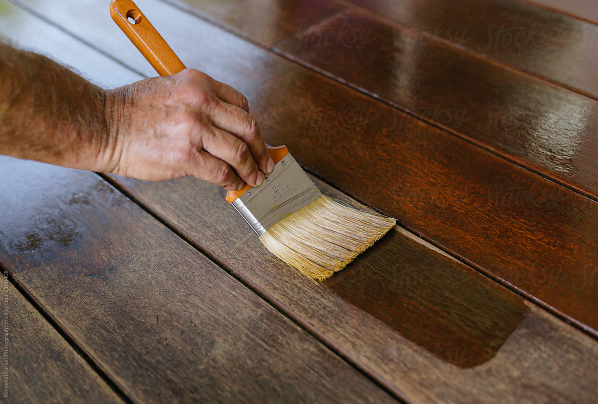 Hand with Paintbrush applying stain to Harwood deck