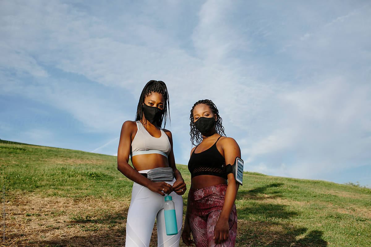 Two women friends on sportswear looking at camera outdoors with face masks