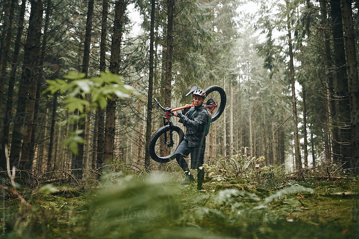 Rider carrying his mountain bike along a forest trail
