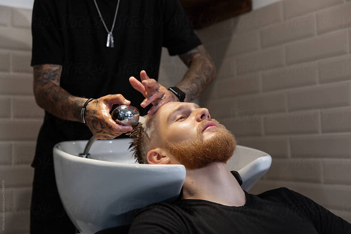 Crop barber washing hair of man in sink