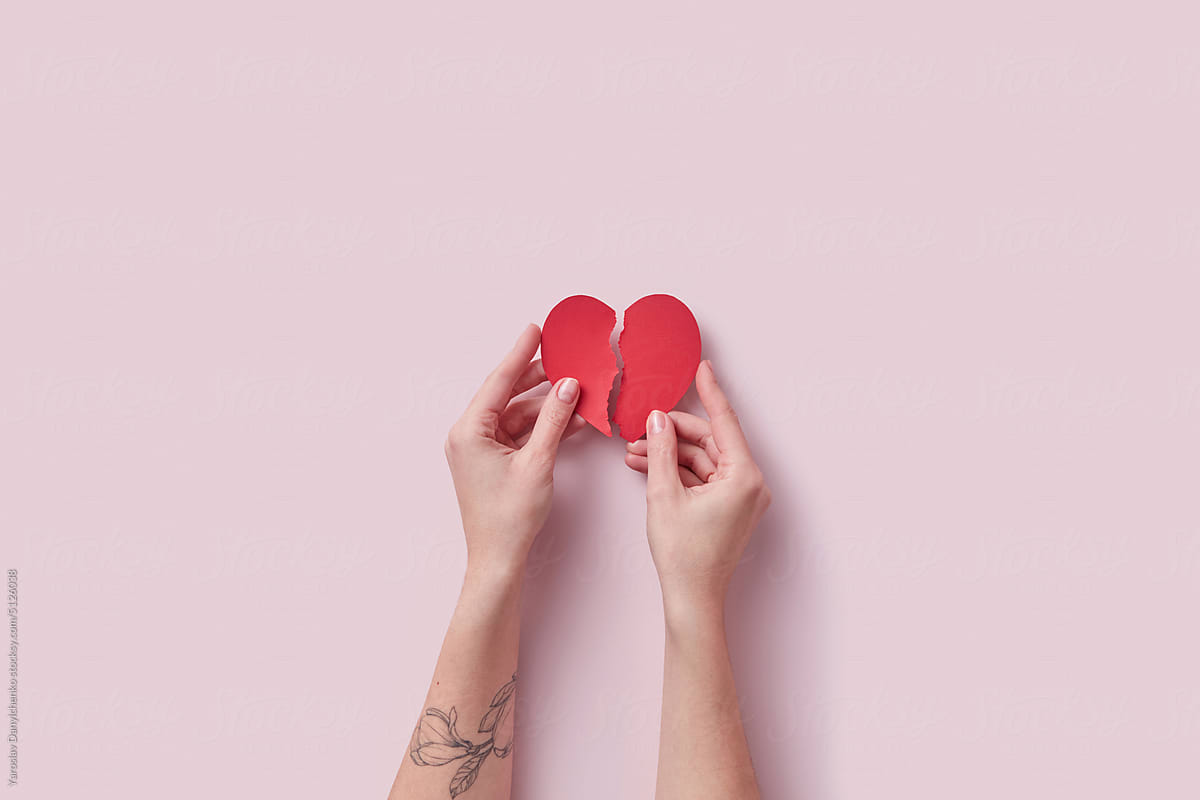 Red torn paper craft heart in tattooed woman's hands.