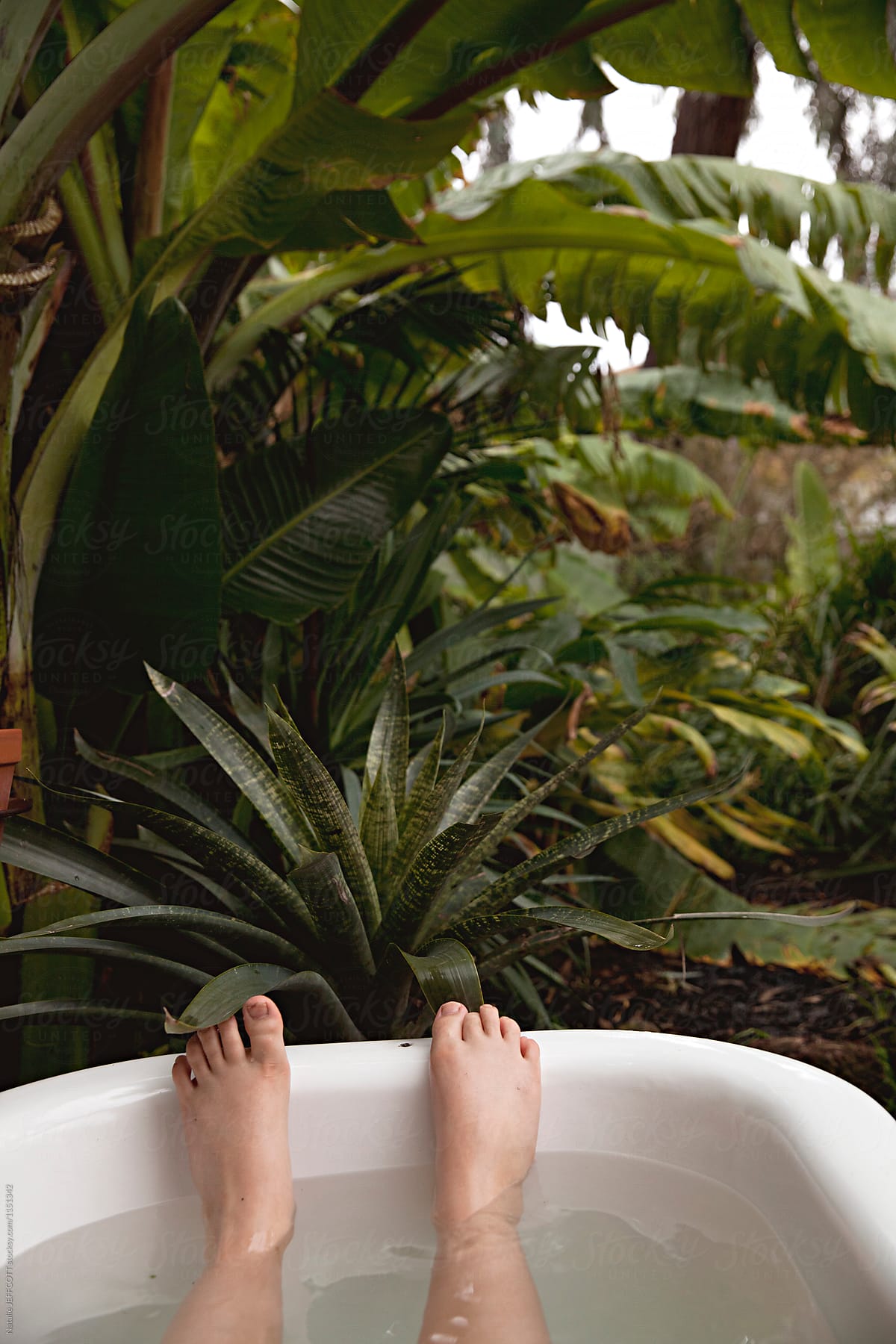 A child\'s feet in a bath in an outdoors tropical garden