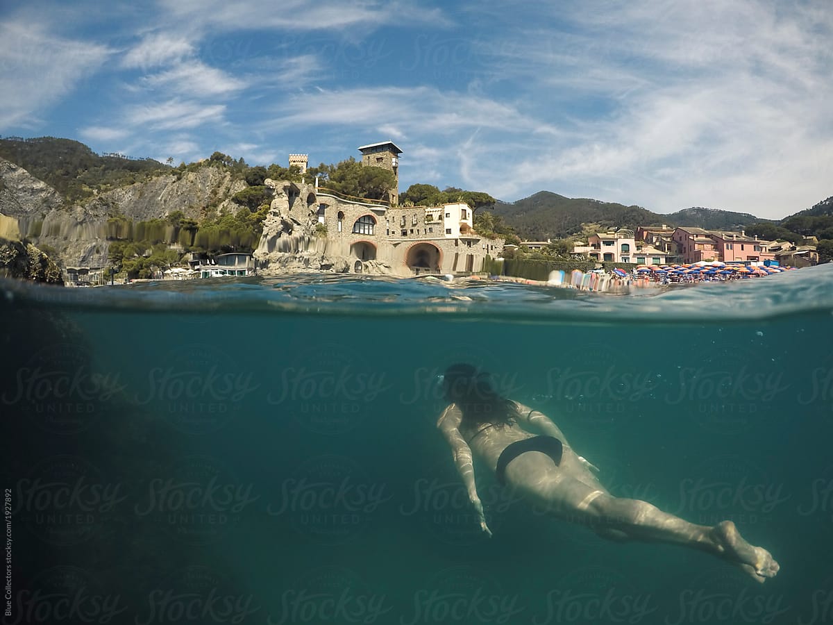 Peaceful woman floating in the water from underwater view and small mediterranean village