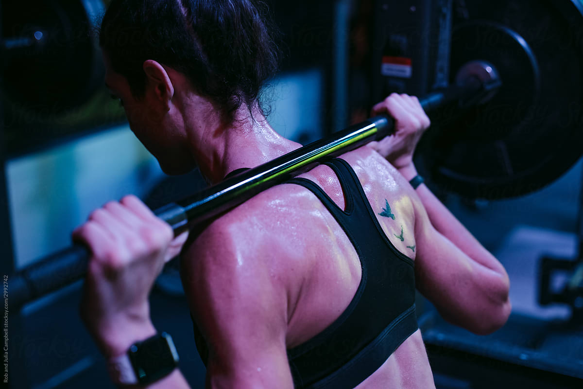 Sweaty athlete woman training hard in dark, moody gym.