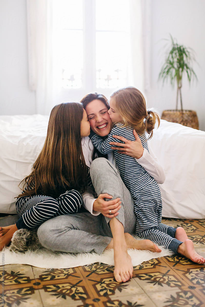 Mom And Her Daughters Kissing And Hugging In The Morning At Home By