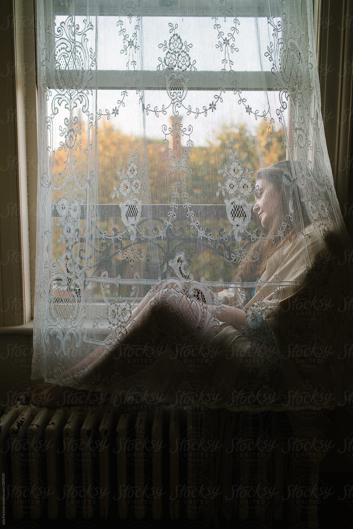 Woman sitting by a window behind a lace curtain.