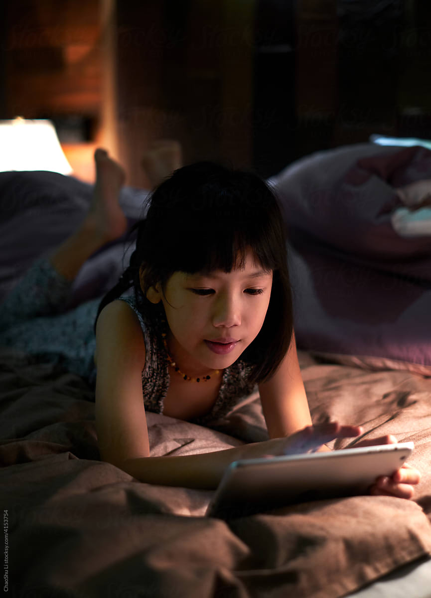 Asian little girl looking at tablet computer on the bed