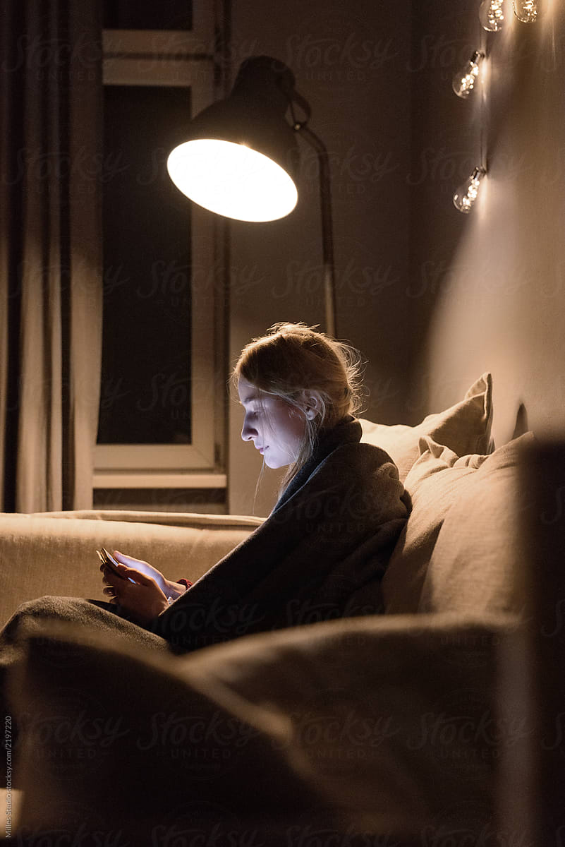 Woman watching tablet on sofa in lamplight