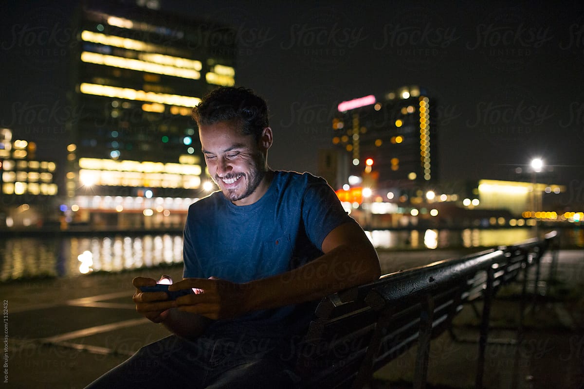 Man using his phone at night, with city lights in the background