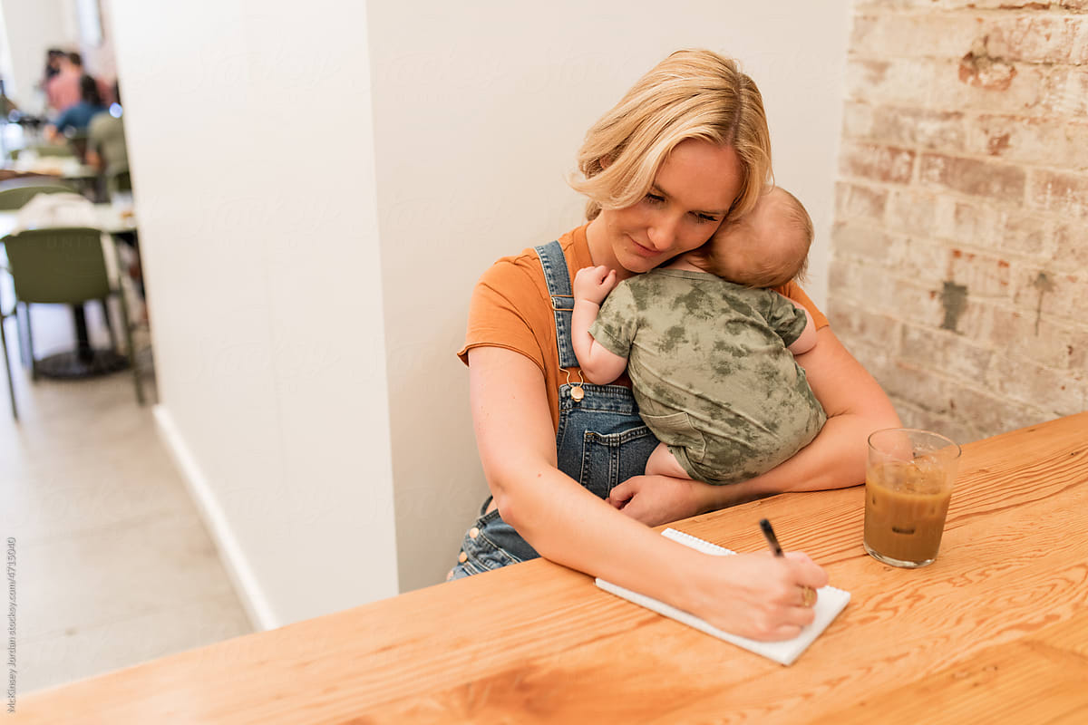Young Mother Writes On Paper While Holding Baby In Arms