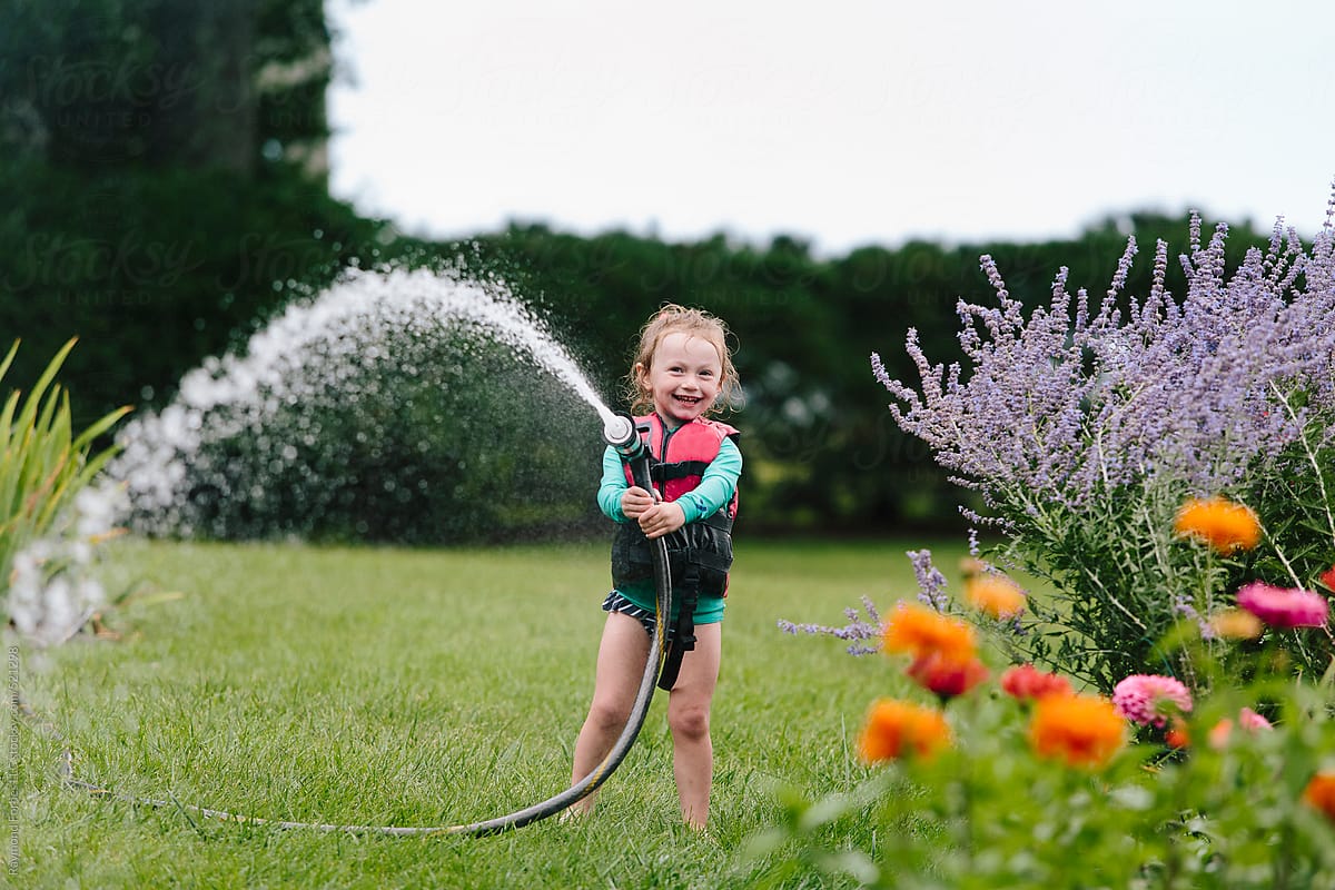 Young girl in backyard playing with water hose and spraying family