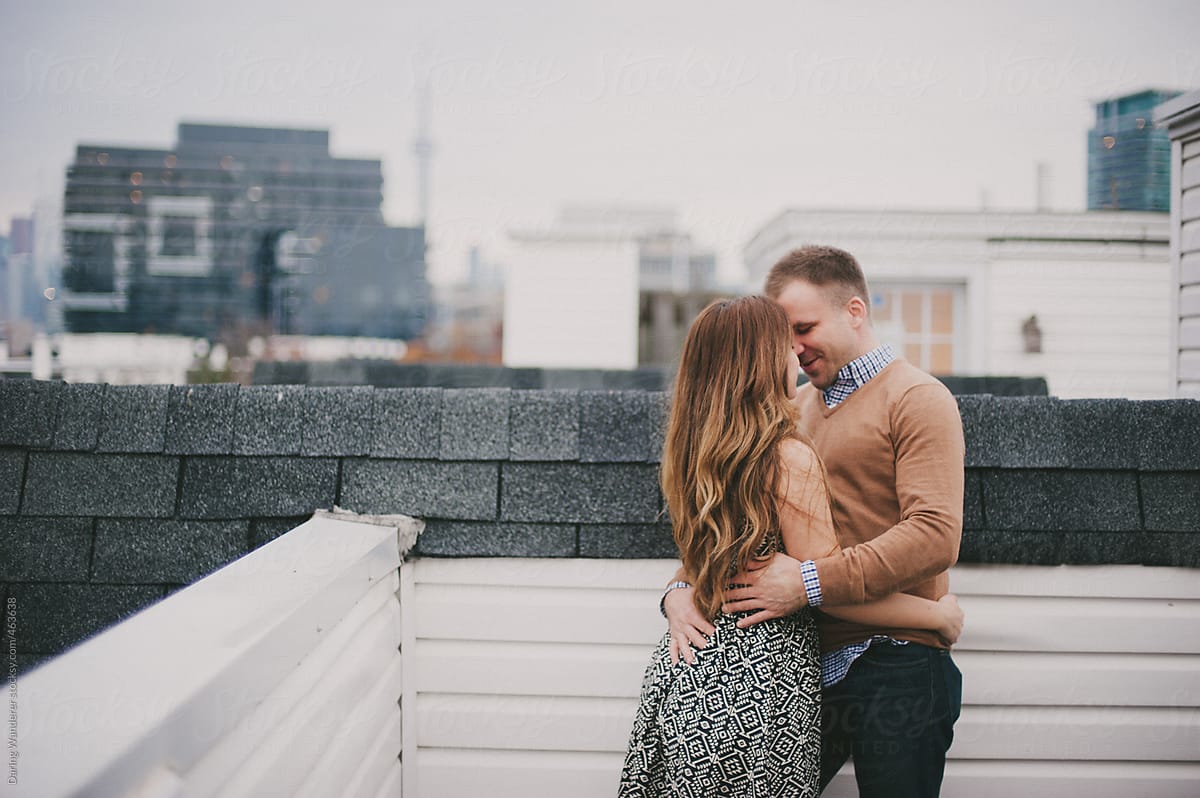 Couple Hugging And Smiling On Rooftop Overlooking Toronto By Stocksy