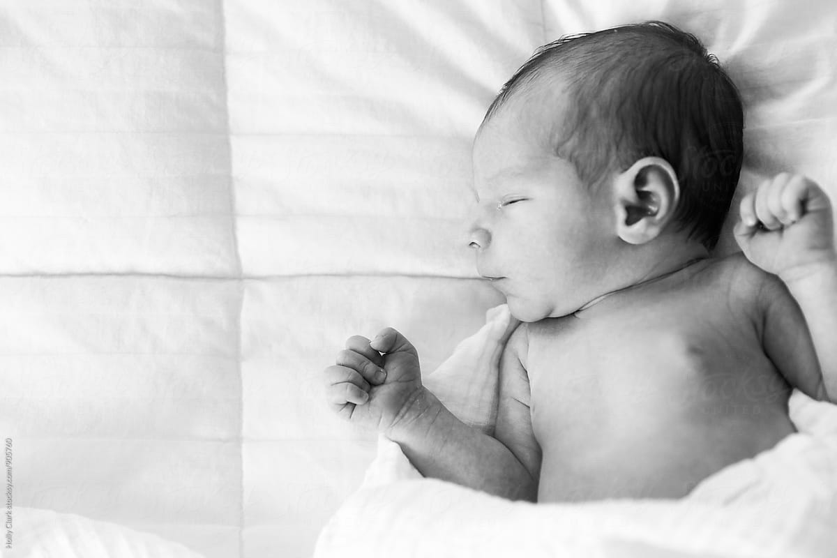 Black and white portrait of baby sleeping on white bed