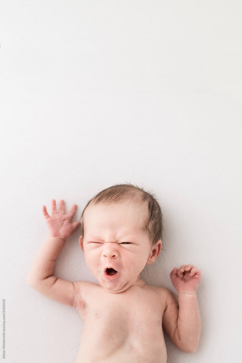 A Newborn Baby Making A Crazy Face While Laying on A White Backdrop