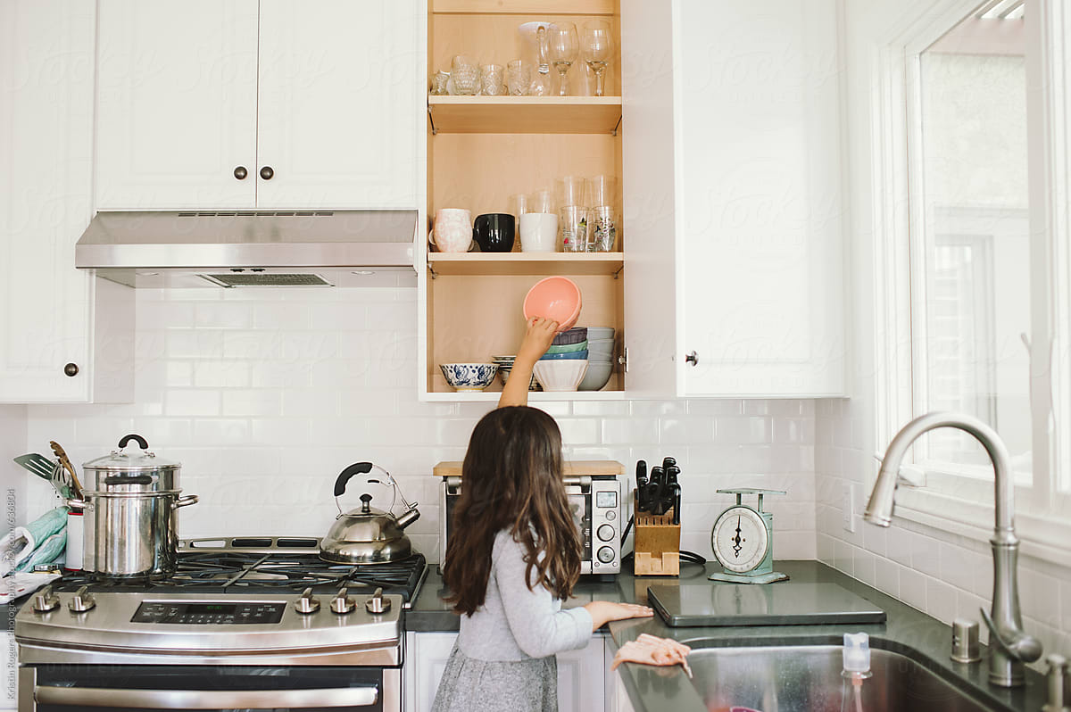Young girl putting dishes away in cupboard in kitchen