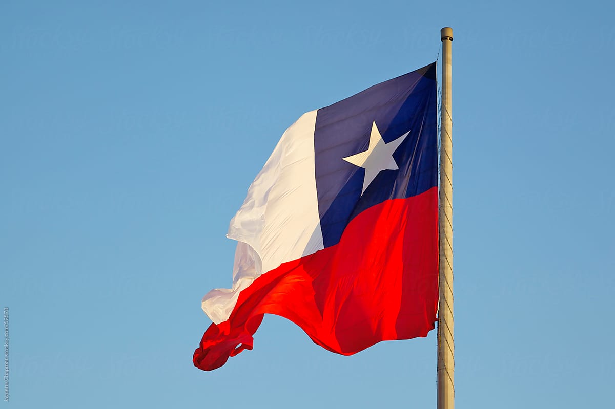 A vibrant Chilean flag blowing in the wind from a flag pole in a blue sky, central Santiago, Chile
