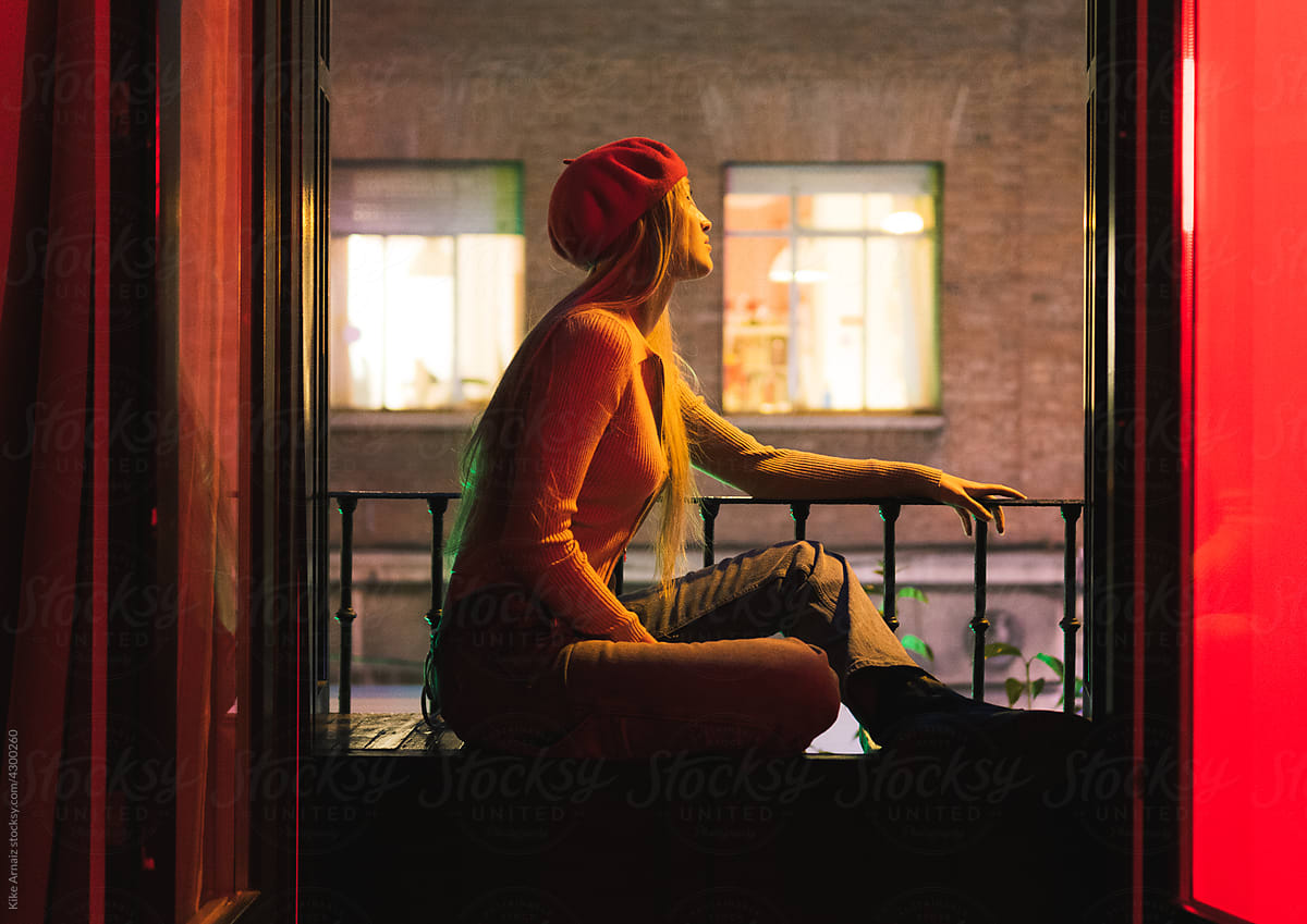 Young woman admiring night street from balcony