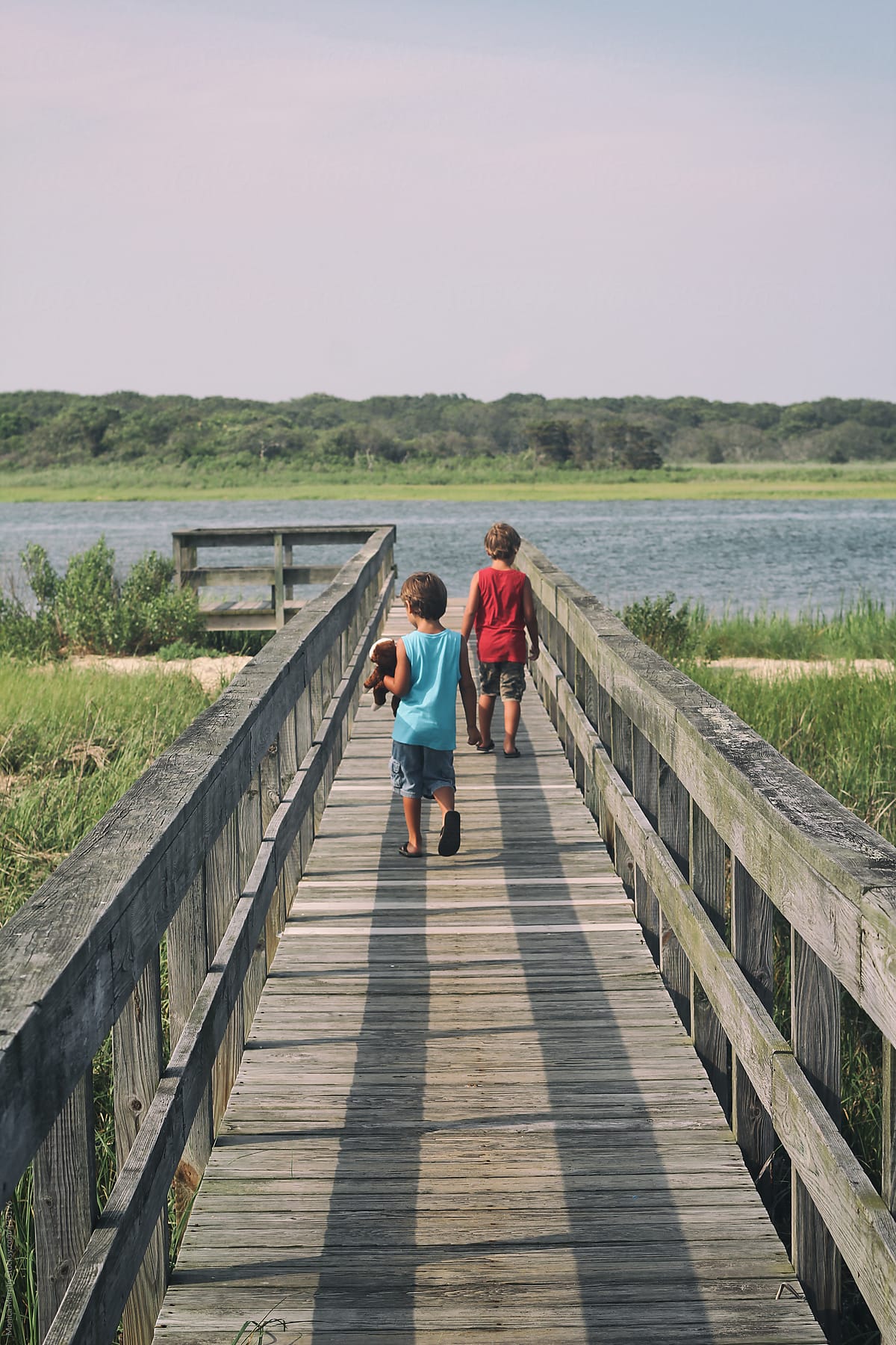 Two young boys walk through marsh on long wooden pier