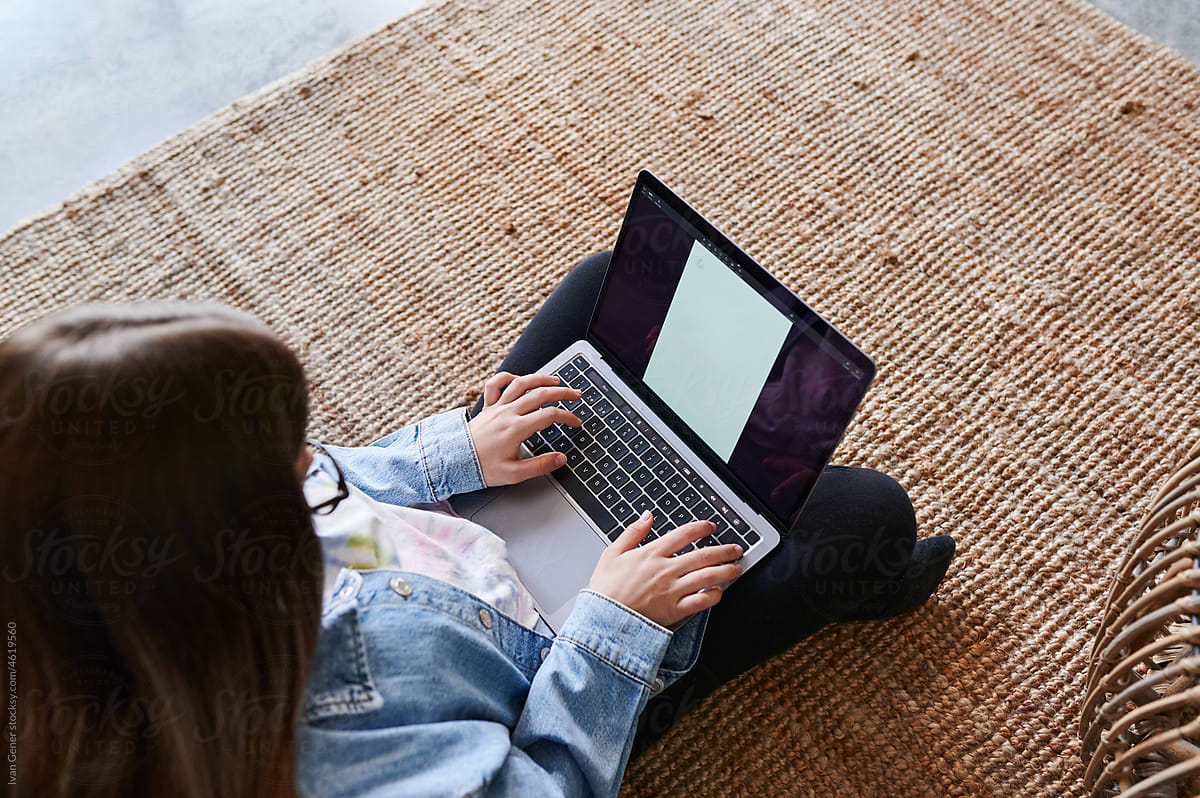 Girl sitting on a floor and doing homework on a laptop