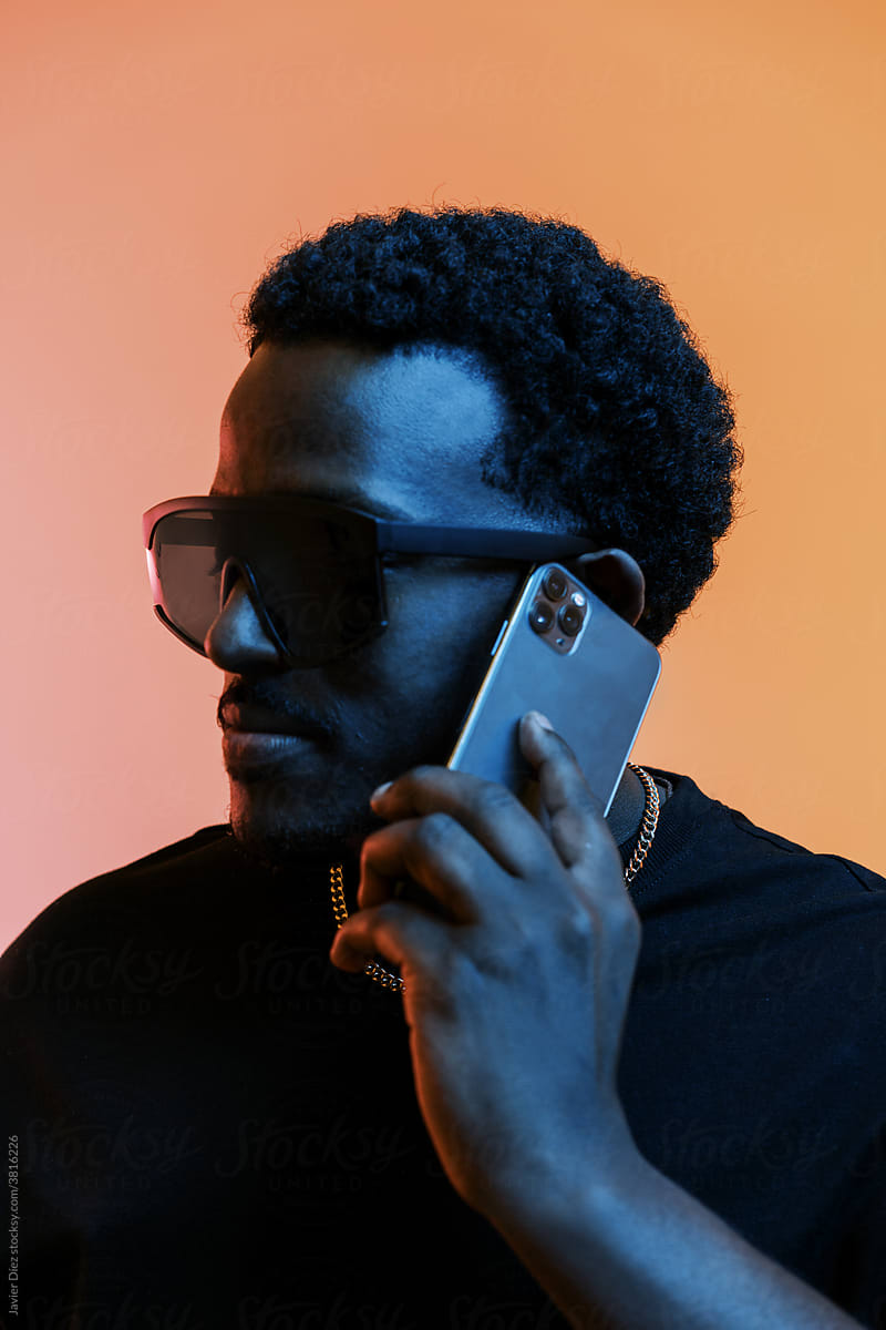 Stylish black man in sunglasses in studio using smartphone