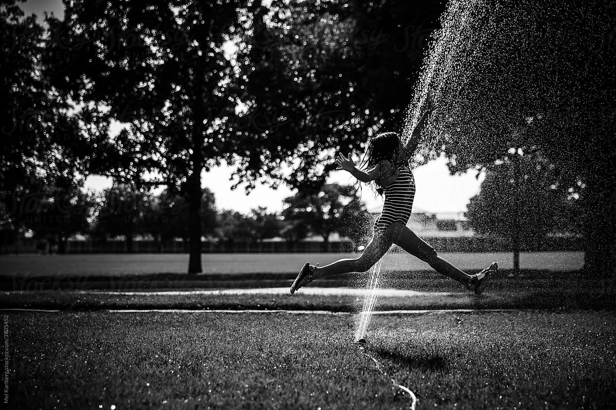 Young girl jumping through a sprinkler