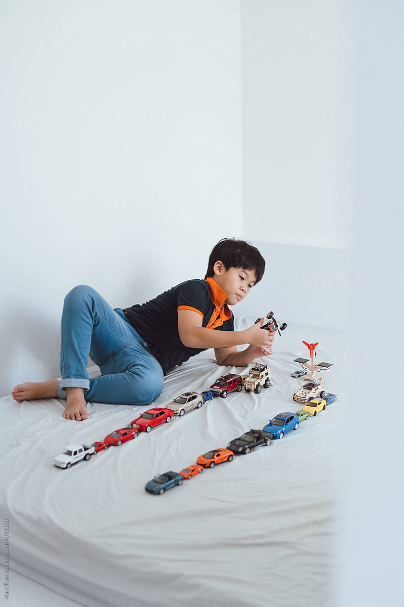 a schoolboy lying on his bed playing with toy cars at home