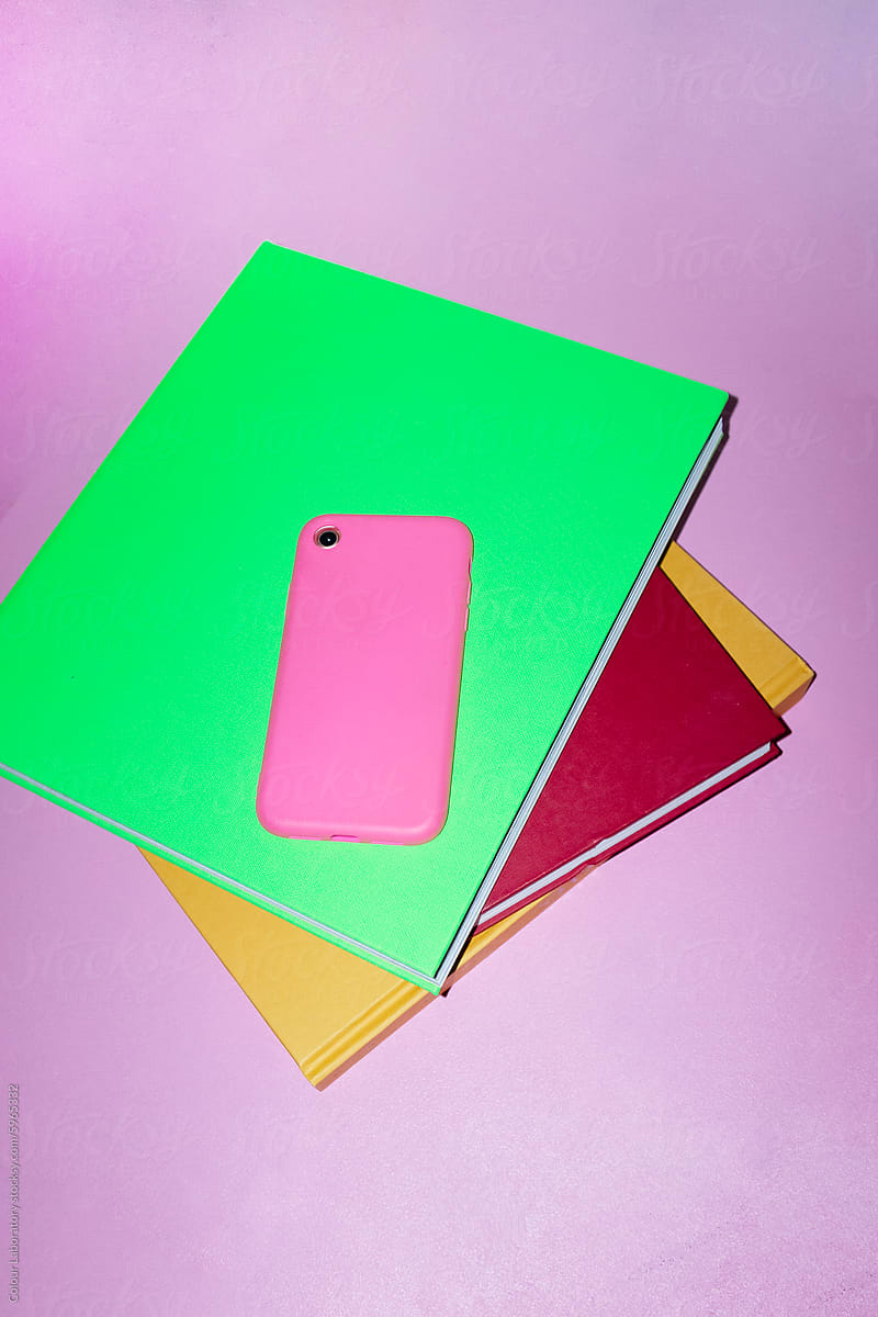 Pink smartphone and colourful books in office with direct flashlight