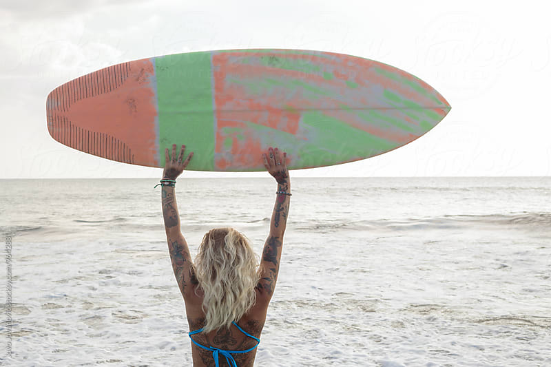 Surfgirl celebrating - holding her surfboard high in the air