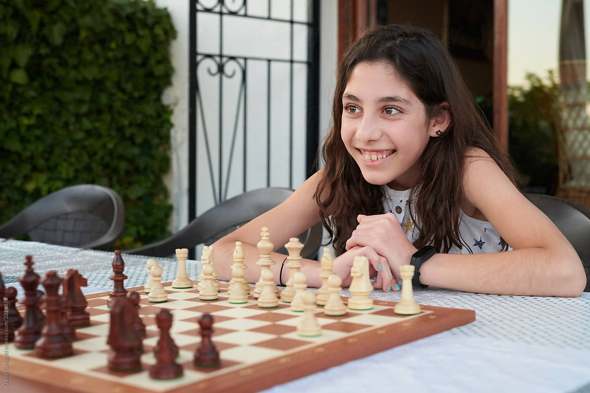 Cheerful girl playing chess in yard
