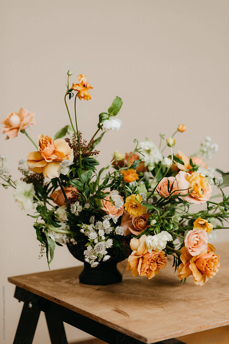 Floral arrangement on wooden table in studio against tan backdrop.