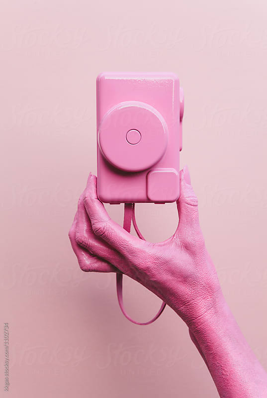 Pink hand holding pink camera over pink background